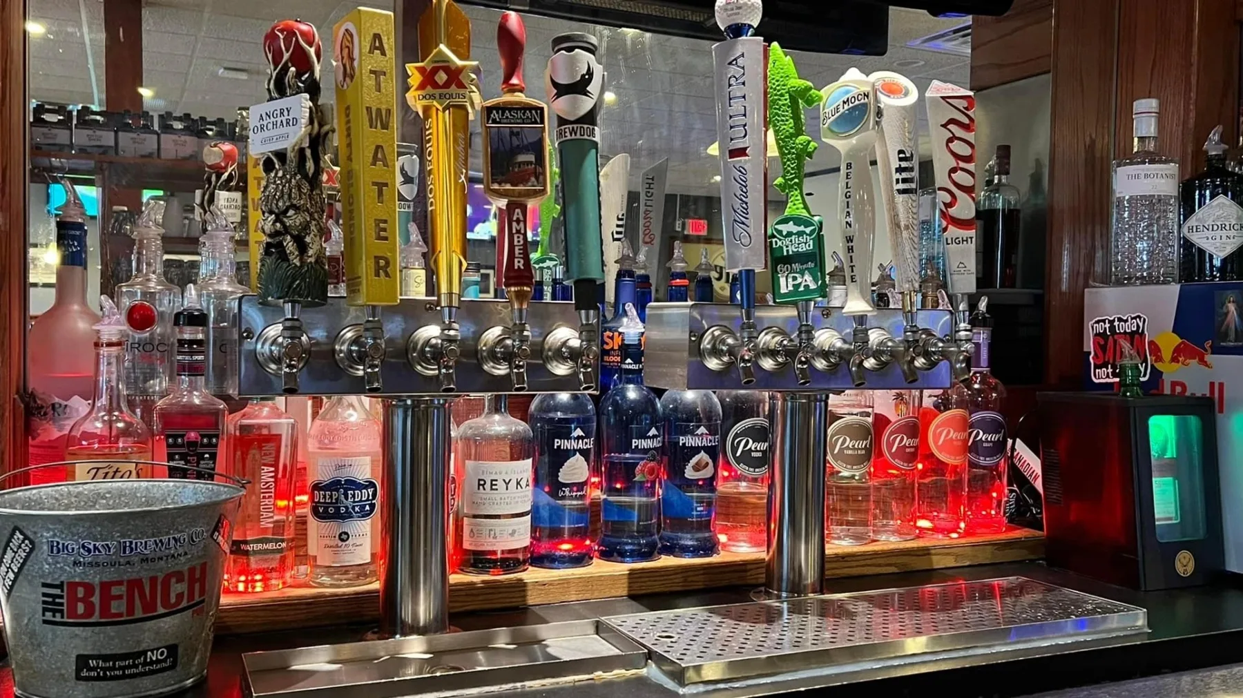 The bar at The Bench Pub with draft taps and bottles lit behind the counter